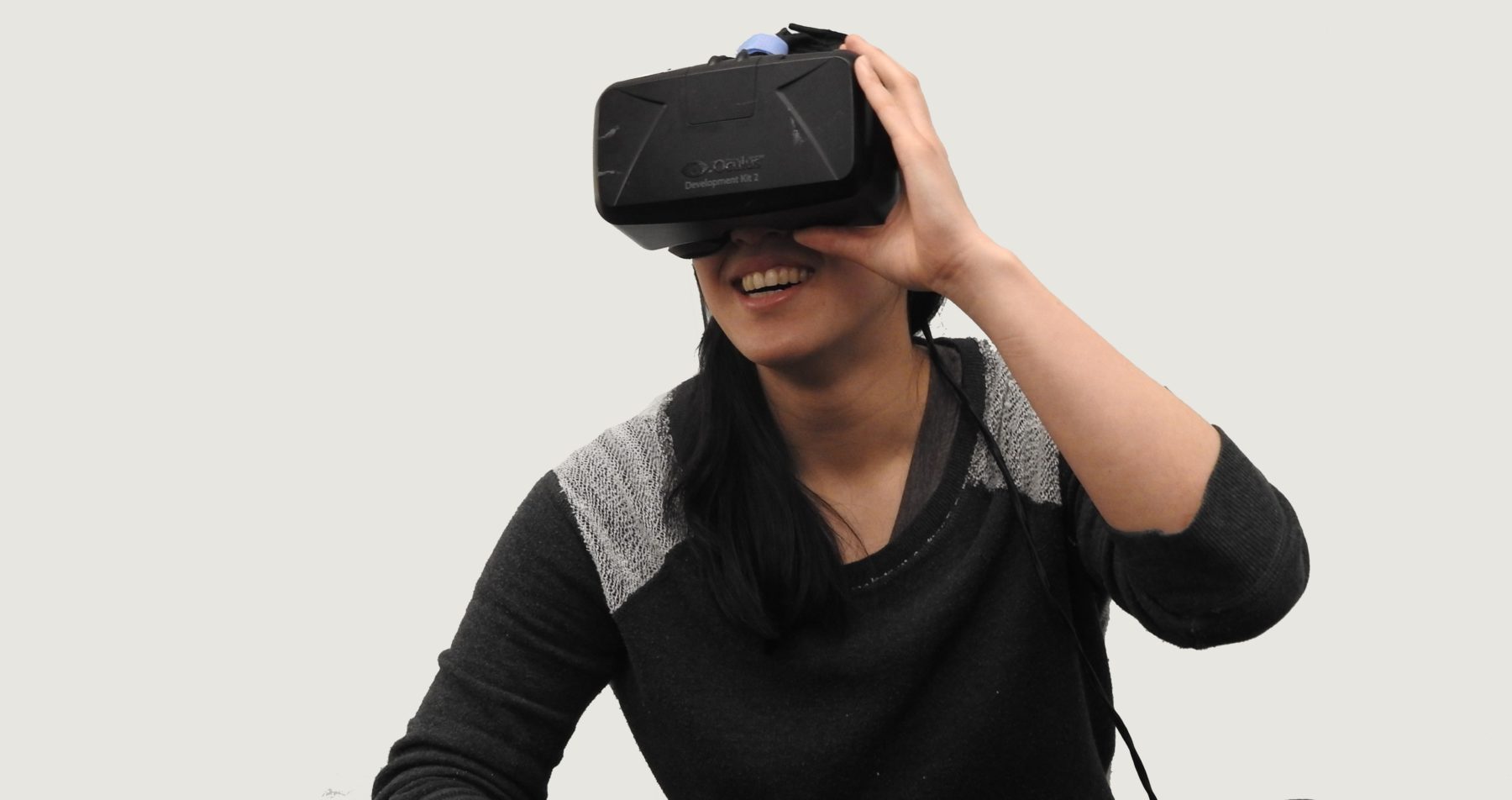 A young woman using a VR head set in a room with white walls.