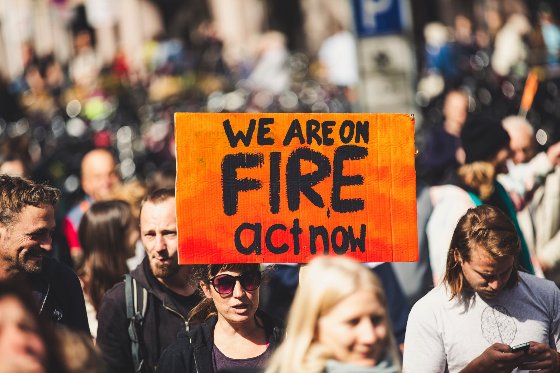 A young woman, at a climate change rally, holding a placard that says "We are on fire act now."