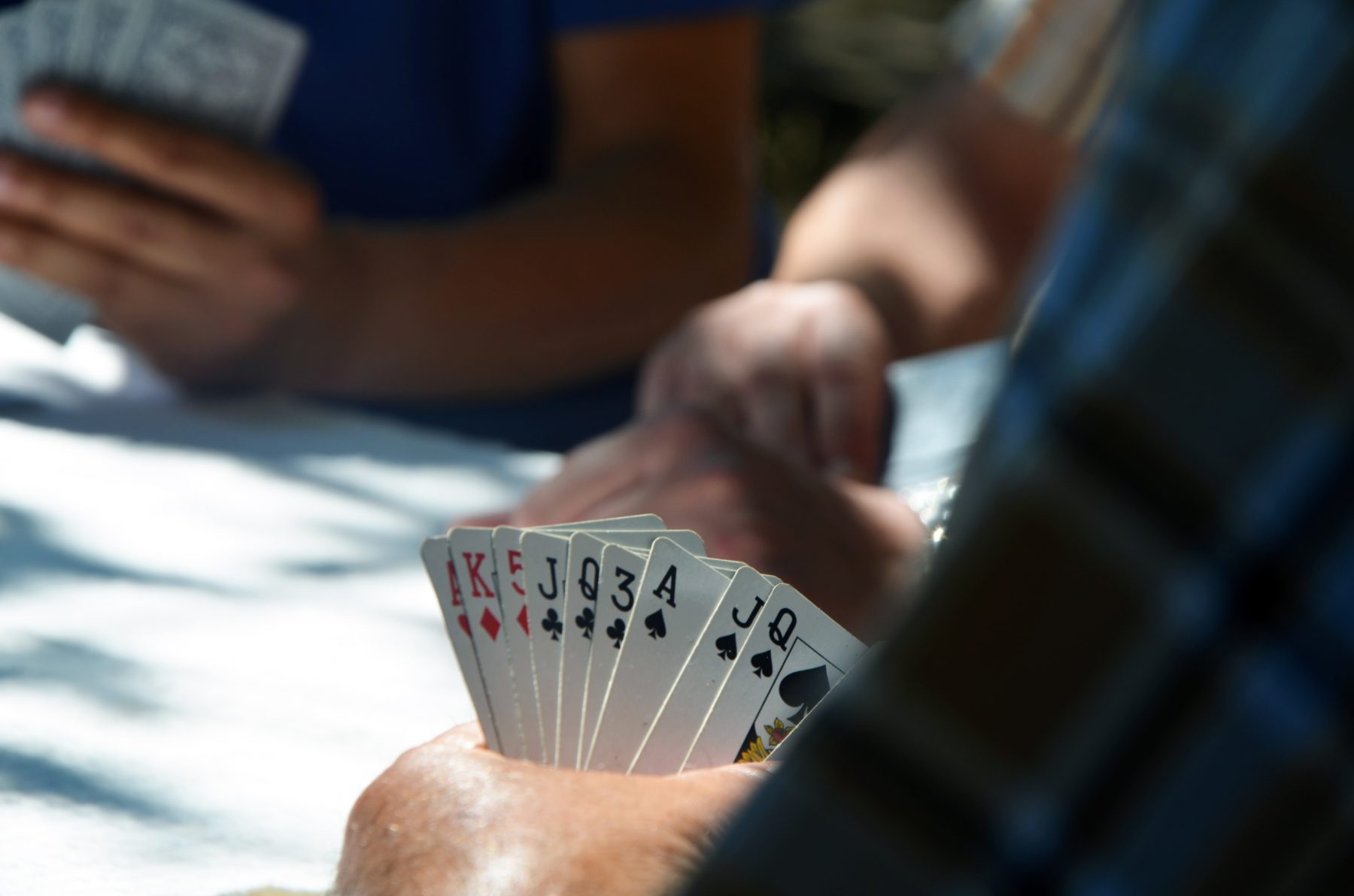 A close up of a person's hand while playing cards at a table with other people.