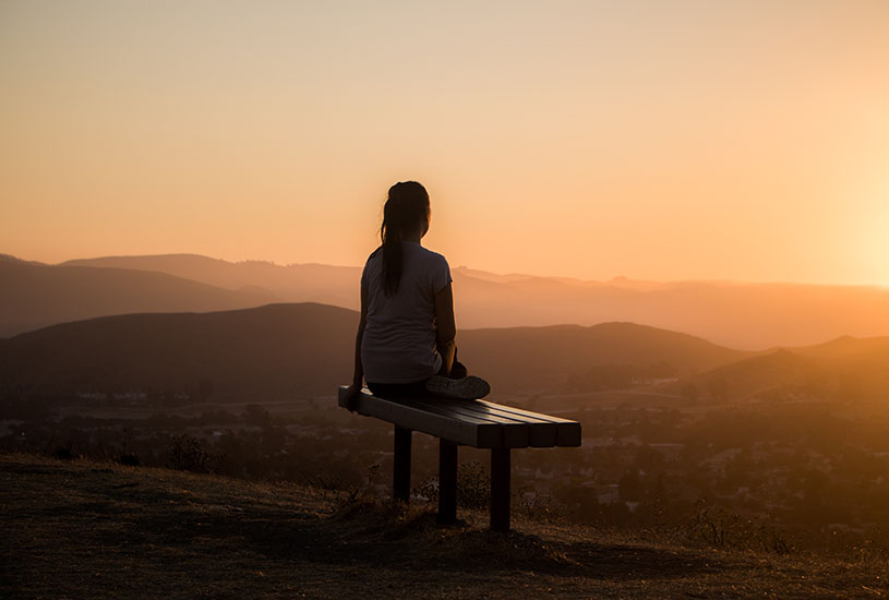 A woman sitting on a bench looking over the landscape.