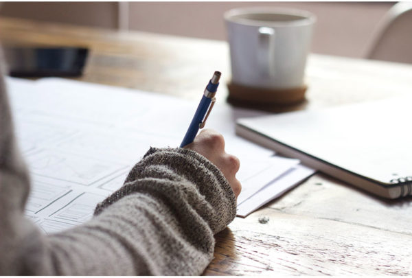 Image of a someone writing on paper, with a coffee cup in the background