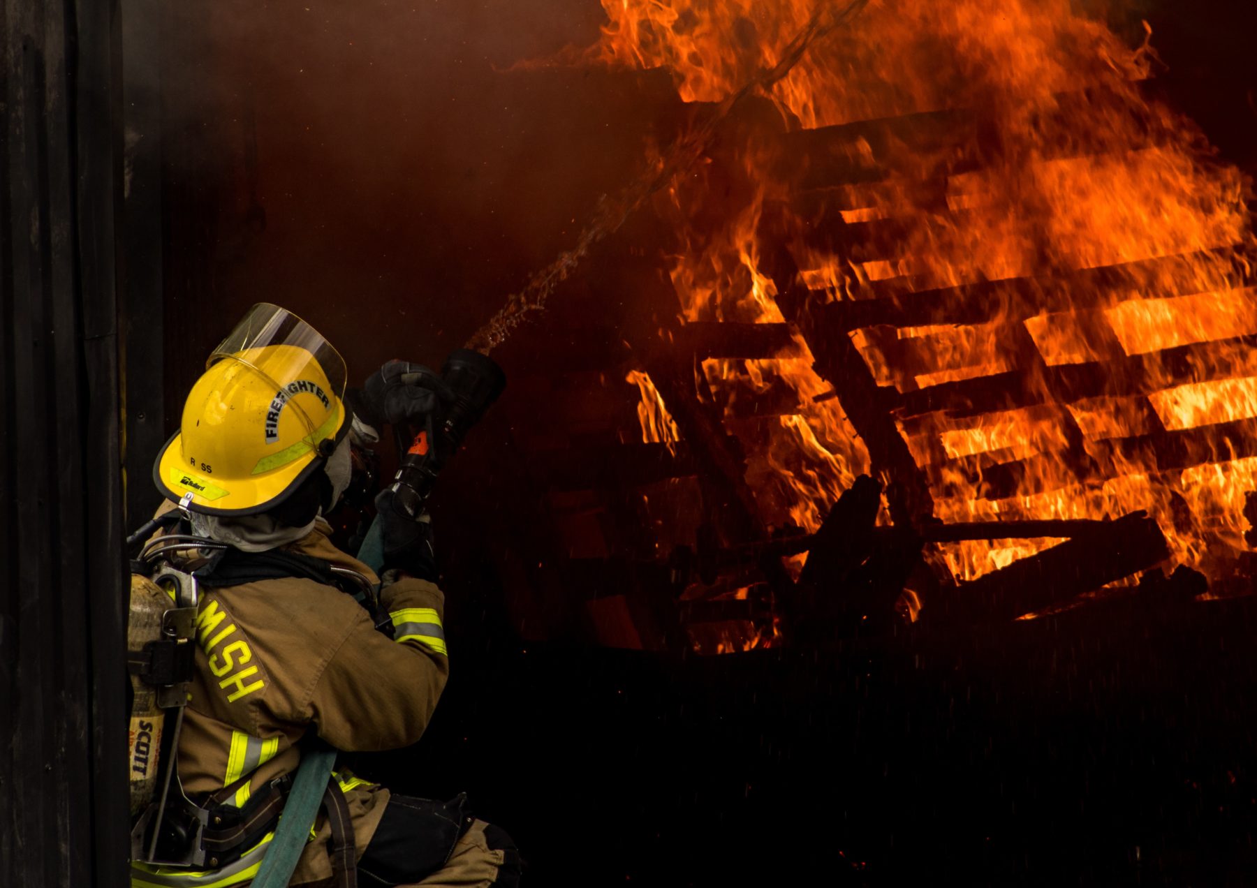 Image of a firefighter spraying water on a pile of burning wood