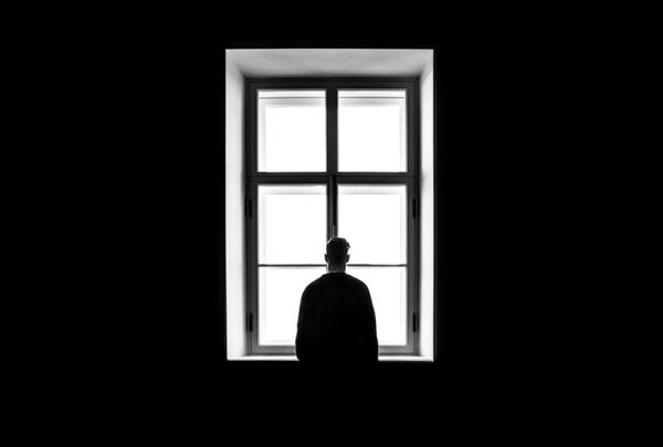 Black and white image of a man staring out a glass window.