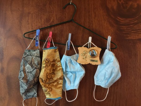 Image of four colourful face masks pegged onto the bottom of a black plastic coat hanger