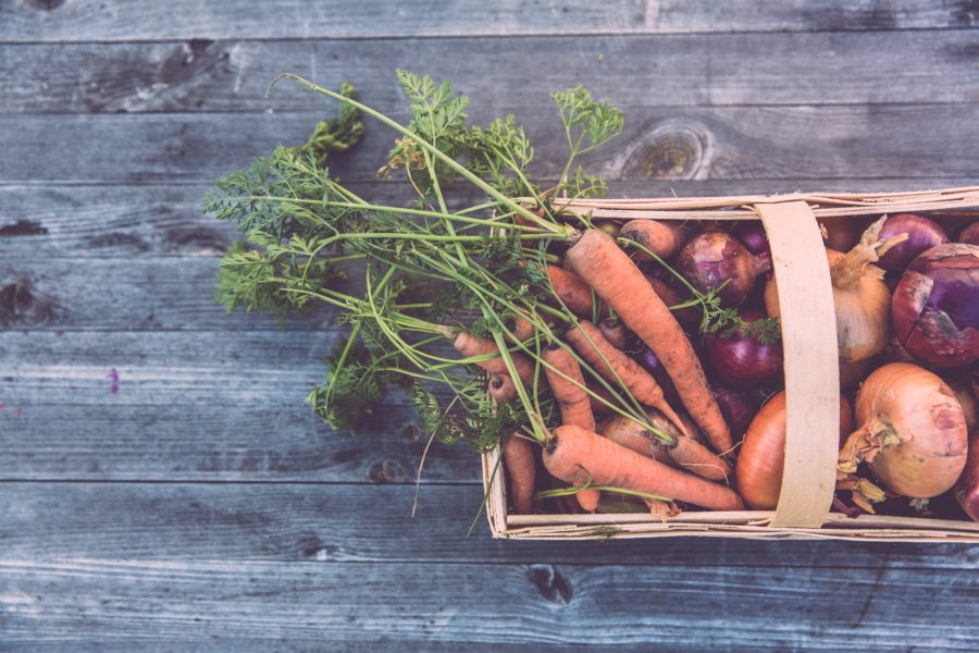 To the right hand side is an overhead view of a wicker basket of carrots, sweet potatoes and beetroot. The basket sits on a grey wood table.