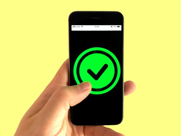 Image of a smartphone on a yellow background. The phone is displaying a green tick